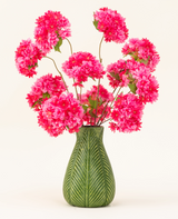 Un jarrón verde con motivo de hojas muestra el ramo de flores artificiales de seda Cherry Blossom Pink (flores de cerezo de seda esponjosas y de color rosa brillante con hojas verdes) sobre un fondo liso y claro.