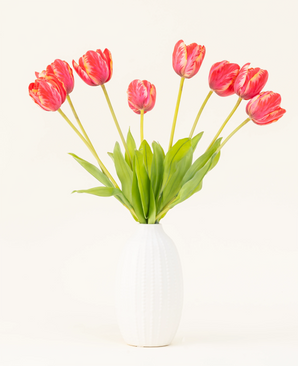 El ramo de flores artificiales de seda Tulipán Francés rojo está dispuesto en un jarrón de cerámica blanca, con ocho tulipanes rojos y amarillos con hojas verdes sobre un fondo liso y claro.