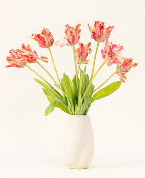 Un jarrón con estructura blanca muestra el ramo de flores artificiales de seda Tulipán Perico Francés rojo/amarillo, con realistas tulipanes rojos y amarillos con hojas verdes sobre un fondo liso y claro.