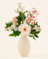 En un jarrón de cerámica de color crema se encuentra el ramo 'Light & Lovely' con flores artificiales de seda de Easyplants, que consta de un arreglo mixto de flores de seda blancas, rosas y violeta claro con hojas verdes, sobre un fondo liso y claro.