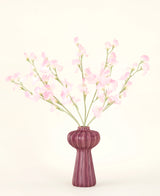 El ramo de flores artificiales de seda Pea rosa claro, con varios tallos de guisantes de color rosa claro en un jarrón acanalado de color burdeos, se alza sobre un fondo pálido: ideal para cualquier interior de flores artificiales.