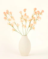 El jarrón de cerámica de color crema contiene el ramo de flores artificiales Silk Pea Peach, con delicadas flores color melocotón y rosa claro con largos tallos verdes sobre un fondo claro y neutro.