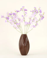 Un jarrón marrón texturizado sostiene el ramo de flores de seda artificial, flores de seda de color violeta claro con tallos verdosos sobre un fondo liso y claro.