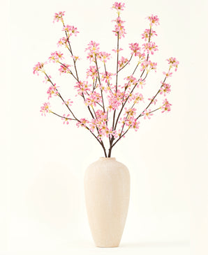 Un jarrón alto de cerámica beige contiene varias ramas del ramo de flores artificiales Silk Flores rosas, con delicadas flores rosas y hojas verdes, sobre un fondo blanco liso.