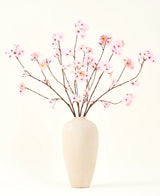 El ramo de flores artificiales de seda Flor de cerezo rosa 114 cm tiene ramas largas y delgadas con racimos de flores de color rosa claro en un jarrón de cerámica beige, que forman un llamativo contraste con el fondo blanco liso.