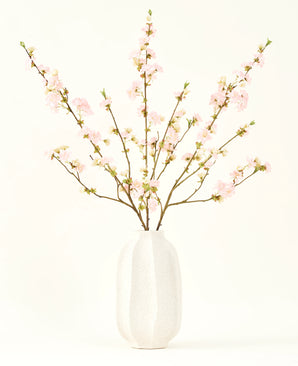 El ramo de flores artificiales de seda Flor de cerezo rosa claro de 94 cm presenta delicadas flores de cerezo artificiales de color rosa en un jarrón de cerámica blanca, que añade elegancia sobre un fondo claro y liso.