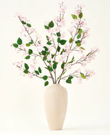 Un jarrón de cerámica beige contiene varias ramas largas con el ramo de flores artificiales Silk de hojas rosas y verdes de Peach Blossom, sobre un fondo blanco liso, perfecto para un interior floral artificial.