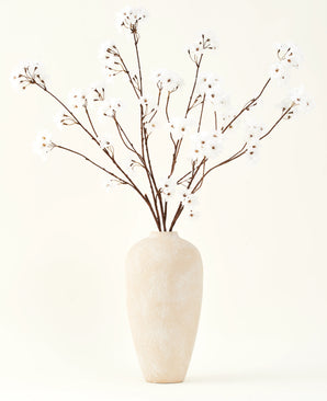 El ramo de flores artificiales de seda Crema de cerezo de 114 cm de altura se encuentra en un jarrón de cerámica beige y aporta una decoración serena a cualquier habitación con sus delicadas ramas de color crema sobre un fondo claro.