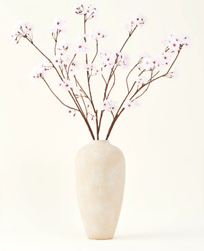 El ramo de flores artificiales de seda Flor de cerezo rosa claro de 114 cm se encuentra en un jarrón alto de cerámica beige con ramas largas y delgadas y delicadas flores de color rosa claro, creando un sereno acento floral artificial sobre un fondo liso.