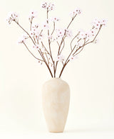 El ramo de flores artificiales de seda Flor de cerezo rosa claro de 114 cm se encuentra en un jarrón alto de cerámica beige con ramas largas y delgadas y delicadas flores de color rosa claro, creando un sereno acento floral artificial sobre un fondo liso.