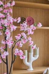 La 'Flor de cerezo artificial' (150 cm) con ramas rosas se coloca delante de estantes de madera, en los que se colocan velas verdes en un candelabro blanco y platos decorativos.