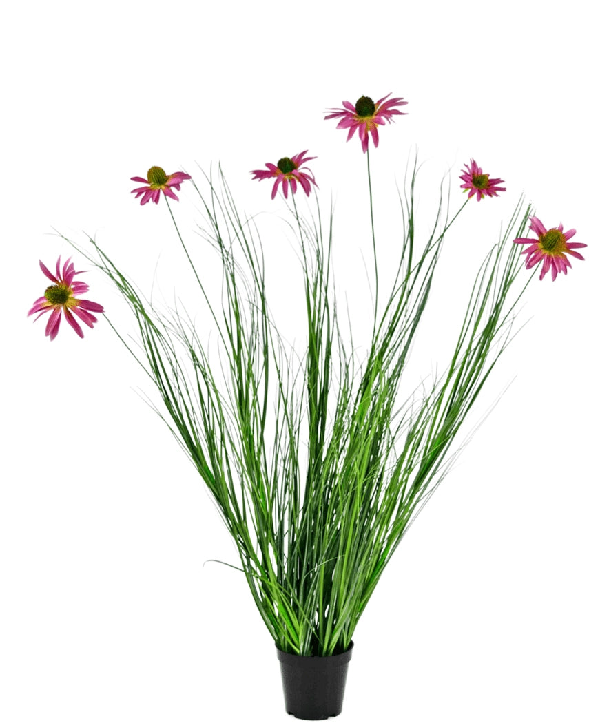 La Planta Césped Artificial Crisantemo 100 cm ignífugo es una planta en maceta con largas hojas verdes y largos tallos rematados con flores de color rosa brillante que parecen margaritas, sobre un fondo blanco.