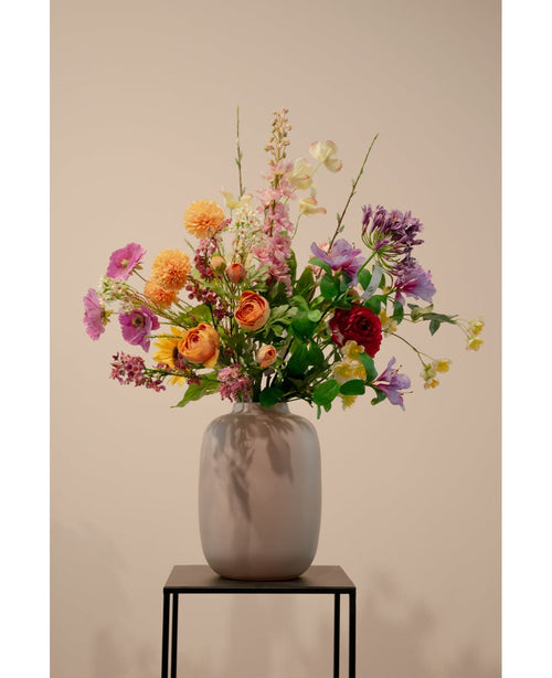 El Cornejo Artificial Real Touch Amarillo Claro 74 cm, una flor artificial realista de color amarillo claro, se encuentra en un jarrón de cerámica con follaje verde sobre un soporte de metal negro sobre un fondo beige liso.