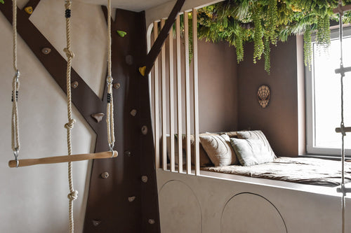 Un acogedor dormitorio infantil con cama empotrada y almohadas está decorado con el seto artificial Lush Deco Deluxe 100x100 cm UV, que añade una exuberante vegetación. Un muro para escalar, una escalera de cuerda y un columpio crean una sensación de casa en un árbol a la luz del día.