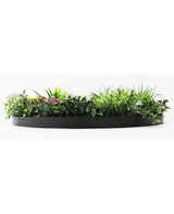 El seto artificial con marco negro Ø100 cm es una jardinera semicircular negra llena de exuberante follaje verde y algunas hojas teñidas de rosa, sobre un fondo blanco.