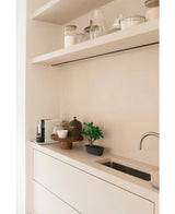 Encimera minimalista con un pequeño fregadero, maceteros decorativos, cafetera y papeleras sobre estantes flotantes. En la combinación de colores neutros blanco y beige, el Bonsái Ficus artificial de 30 cm se utiliza como planta decorativa en maceta.