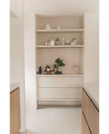 Rincón de cocina minimalista con estantes de madera clara con macetas, jarrones, decoración, una encimera con pequeños electrodomésticos y la maceta Bonsai Artificial Juniper de 40 cm, además de cajones empotrados y un pequeño grifo, todo en tonos neutros.