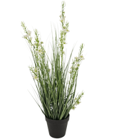 La maceta de césped artificial Mijo Cebolla ignífuga de 65 cm tiene hojas altas y delgadas de color verde similar a la hierba y varios tallos con pequeñas flores blancas en una maceta negra, sobre un fondo blanco liso.