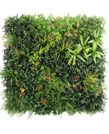 El seto artificial Marisa 100x100 cm UV es una pared verde exuberante y cuadrada con plantas de follaje mixto, helechos, detalles en amarillo verdoso y hojas parduscas dispersas sobre un fondo blanco liso.