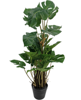 La Planta Artificial Monstera 90 cm es una planta artificial con grandes hojas de color verde brillante con divisiones naturales, erguida en una maceta negra sobre un fondo liso blanco.
