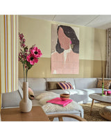 Una sala de estar moderna con un sofá modular, un arreglo floral rosa de hierba gatera artificial (75 cm) en un jarrón, una manta esponjosa y una pintura mural abstracta de una mujer. El interior se caracteriza por colores suaves y detalles estampados.