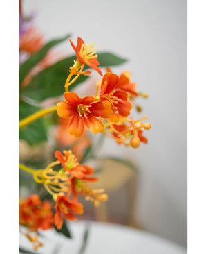 Primer plano de la rama artificial Daphne Spray de 108 cm en color naranja vibrante, con hojas verdes realistas y estambres amarillos, sobre un fondo suavemente descolorido.