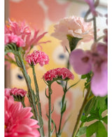 Un primer plano de las flores artificiales rosas Statice de 64 cm, que presentan delicadas flores estáticas rosas sobre un fondo pastel borroso con formas abstractas en amarillo y melocotón.