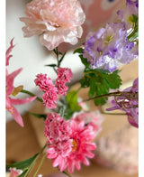 Un primer plano de la rama artificial Statice de 64 cm de color rosa, con delicadas flores rosas y hojas verdes, dispuestas en un ramo sobre un fondo interior suavemente descolorido.