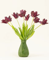 De Zijden kunstbloemen boeket Franse Parkiet Tulp paars heeft donkerpaarse, gefranjerde tulpen met lange groene stelen in een vaas met groen bladmotief, waardoor een opvallende display tegen een witte achtergrond ontstaat.
