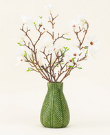 Een groene vaas toont het Zijden kunstbloemen boeket Magnolia wit, met verschillende witte magnoliatakken met kleine groene blaadjes, tegen een effen lichte achtergrond.