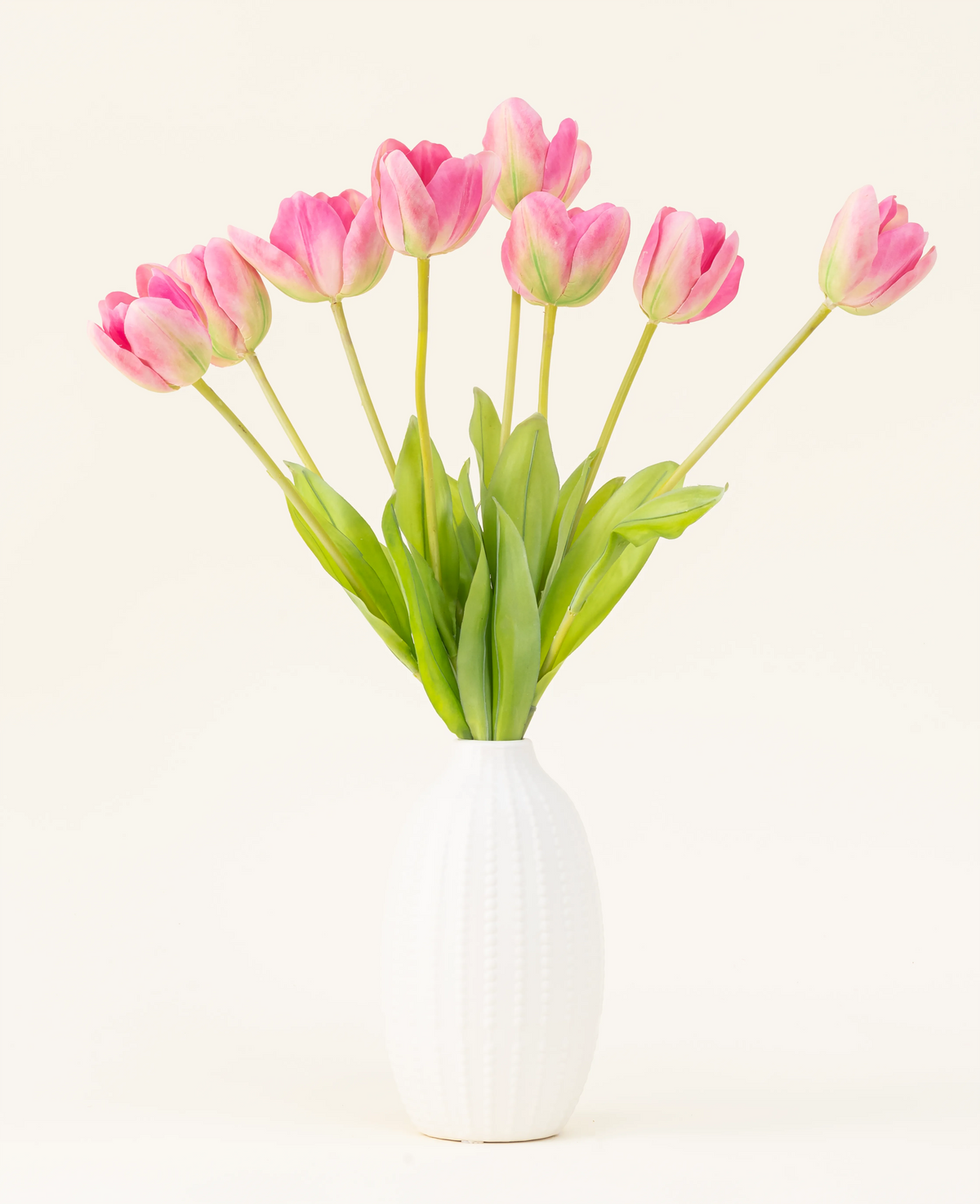 El ramo de flores artificiales de seda French Tulip rosa está dispuesto en un jarrón blanco, con tulipanes franceses rosas y hojas verdes sobre un fondo claro y sencillo.