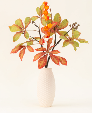 El ramo de flores artificiales de seda Autumn Flair tiene un jarrón con estructura blanca y rama tipo farol, flores naranjas en forma de farol y hojas verde-rojas, que forman un elegante decorado otoñal sobre un fondo liso y claro.
