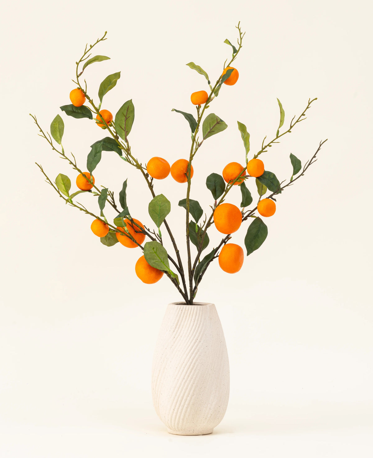 El ramo de flores artificiales de seda mandarina tiene un jarrón con textura blanca y ramas de hojas verdes y mandarinas artificiales de color naranja vibrante, que añaden un toque animado sobre un fondo claro y liso.