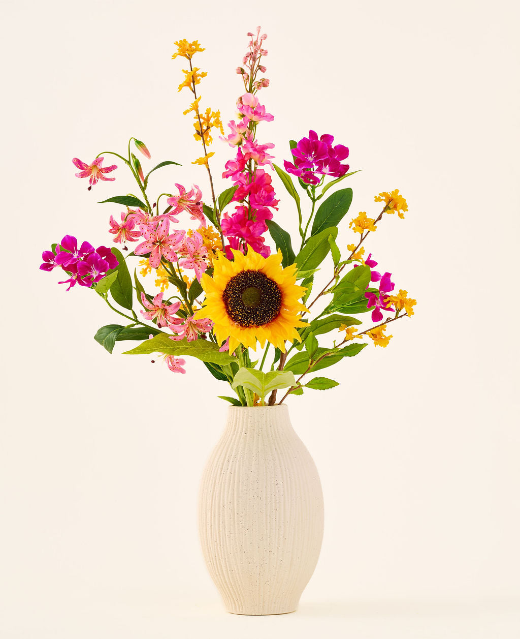 El ramo de flores artificiales de seda 'Tiny Sunshine' está colocado en un jarrón de cerámica beige, compuesto por un ramo artificial de flores realistas, como un gran girasol, flores rosas y magentas y flores amarillas con hojas verdes, sobre un fondo liso y claro. Este arreglo de Easyplants consta de hermosas flores de seda que añaden belleza duradera a cualquier habitación.