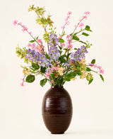 In een donkerbruine vaas staat een boeket van roze, paarse en gele Zijden kunstbloemen, het ‘Sky Kiss’-boeket, met groene bladeren, tegen een effen lichte achtergrond. Deze onderhoudsvrije decoratie zorgt voor blijvende schoonheid in elke ruimte, zonder dat er onderhoud nodig is.