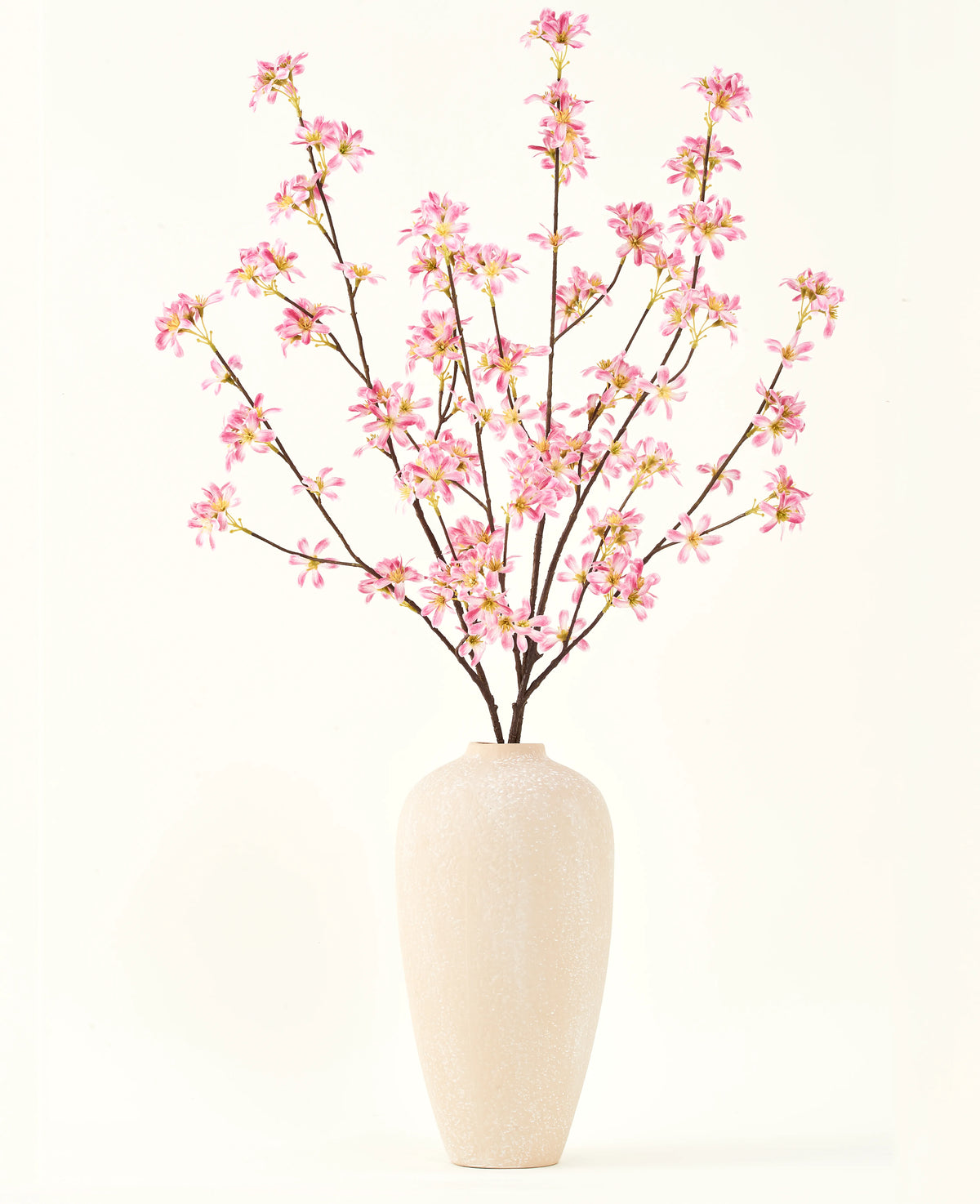 Un jarrón alto de cerámica beige contiene varias ramas del ramo de flores artificiales Silk Flores rosas, con delicadas flores rosas y hojas verdes, sobre un fondo blanco liso.