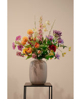 El Cornejo Artificial Real Touch Amarillo Claro 74 cm, una flor artificial realista de color amarillo claro, se encuentra en un jarrón de cerámica con follaje verde sobre un soporte de metal negro sobre un fondo beige liso.