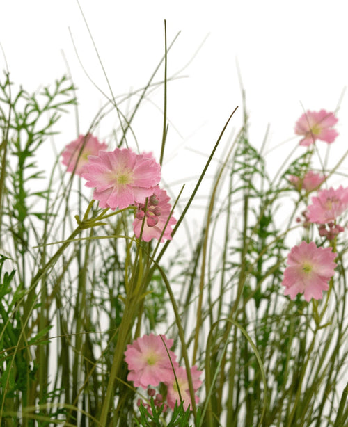 La maceta de césped artificial con flor de Gesang rosa, cebolla, 90 cm, retardante de fuego, tiene flores rosadas con un corazón verde claro que florecen entre hierba alta y delgada y plantas de follaje exuberante, todo sobre un fondo blanco.