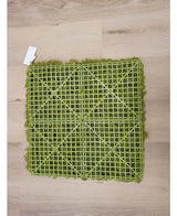 De Kunsthaag Nordic Mos 50x50 cm UV is een groene kunstgrasmat met een zichtbare kunststof rasterrug, ideaal voor luxe interieurs of het creëren van een groene muur. Hij rust op een lichte houten vloer met een klein wit label in een hoek.