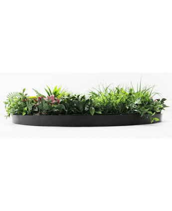 De Kunsthaag op Zwart Frame Ø100 cm is een zwarte, halfronde plantenbak gevuld met weelderig groen gebladerte en enkele roze getinte bladeren, tegen een witte achtergrond.