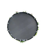 Een Kunsthaag op Zwart Frame Ø100 cm trampoline, van bovenaf gezien met groene bladeren en roze bloemen rond de rand, tegen een witte achtergrond.