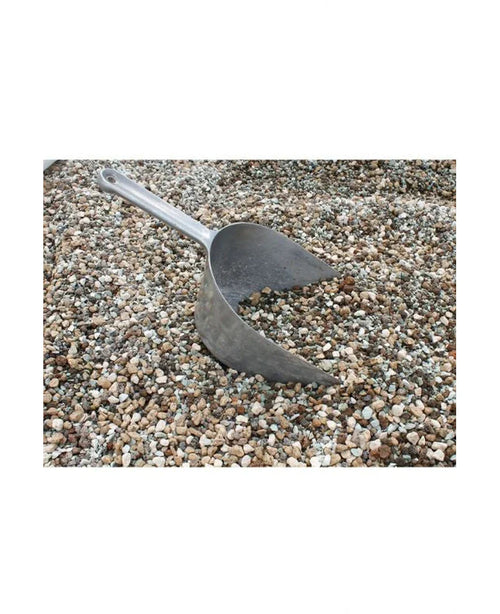 Una pala de metal está parcialmente enterrada en un montón de guijarros volcánicos de una bolsa de 10 litros.