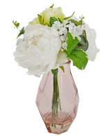Het Kunstboeket in glas 25 cm heeft witte en lichtgroene kunstbloemen met groene bladeren in een roze geometrische glazen vaas, tegen een witte achtergrond.