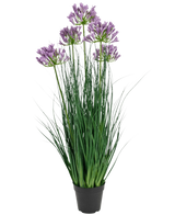 La maceta de césped artificial Agapanthus Onion Grass de color morado es una planta artificial ignífuga de 90 cm de altura con largas hojas verdes y racimos de flores de color violeta, expuestas en una maceta negra lisa sobre un fondo blanco.